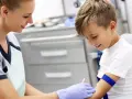 Uśmiechnięta pielęgniarka pobiera krew od chłopca. Wyniki badań wykazały podwyższone płytki krwi, ale chłopiec dzielnie znosi zabieg.