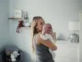 Mama tuli noworodka, by ukoić jego czkawkę. W tle pokój dziecięcy z pluszakami.