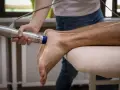 Fizjoterapeuta stosuje falę uderzeniową na stopę pacjenta, by leczyć uciążliwe ostrogi.