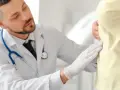 Lekarz w białym fartuchu i rękawiczkach bada pacjenta.