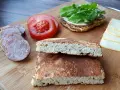 Chleb keto, plasterki kiełbasy, pomidor i ser na desce. Idealne składniki na keto kanapkę.