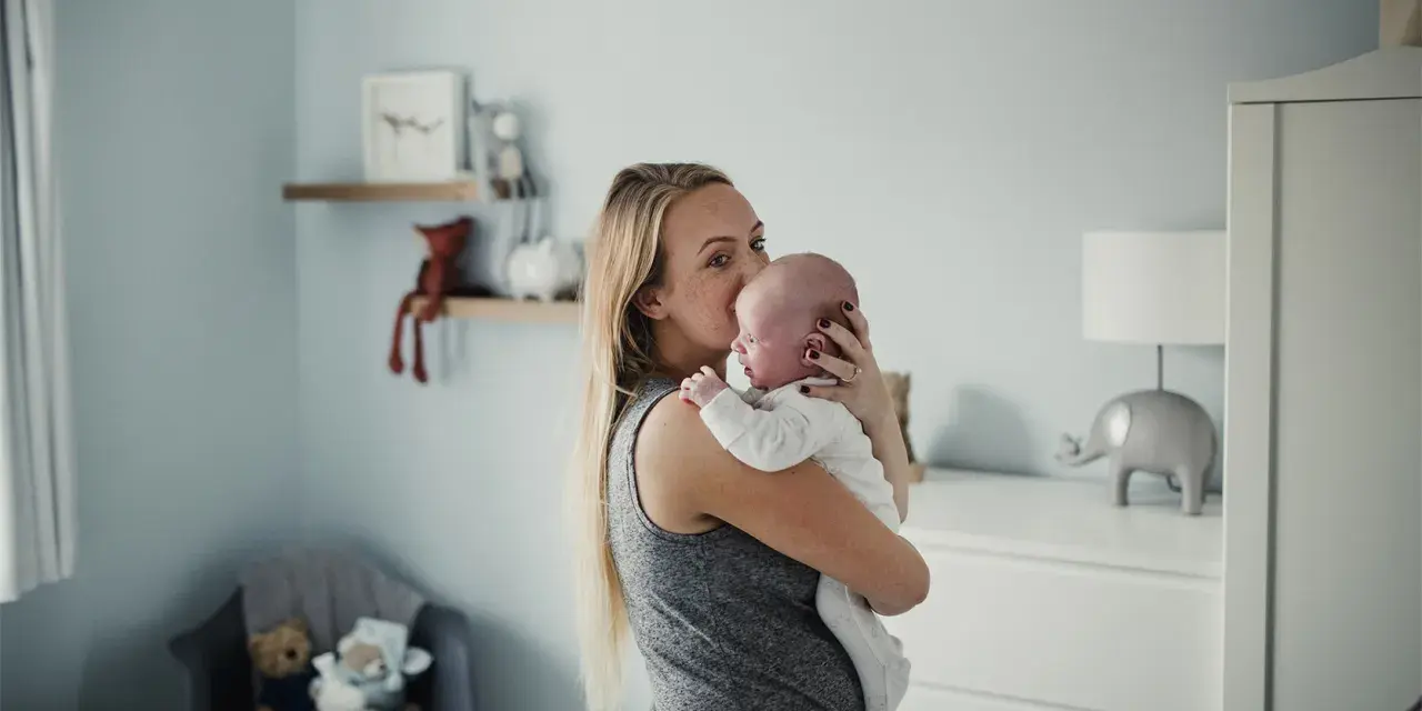 Mama tuli noworodka, by ukoić jego czkawkę. W tle pokój dziecięcy z pluszakami.