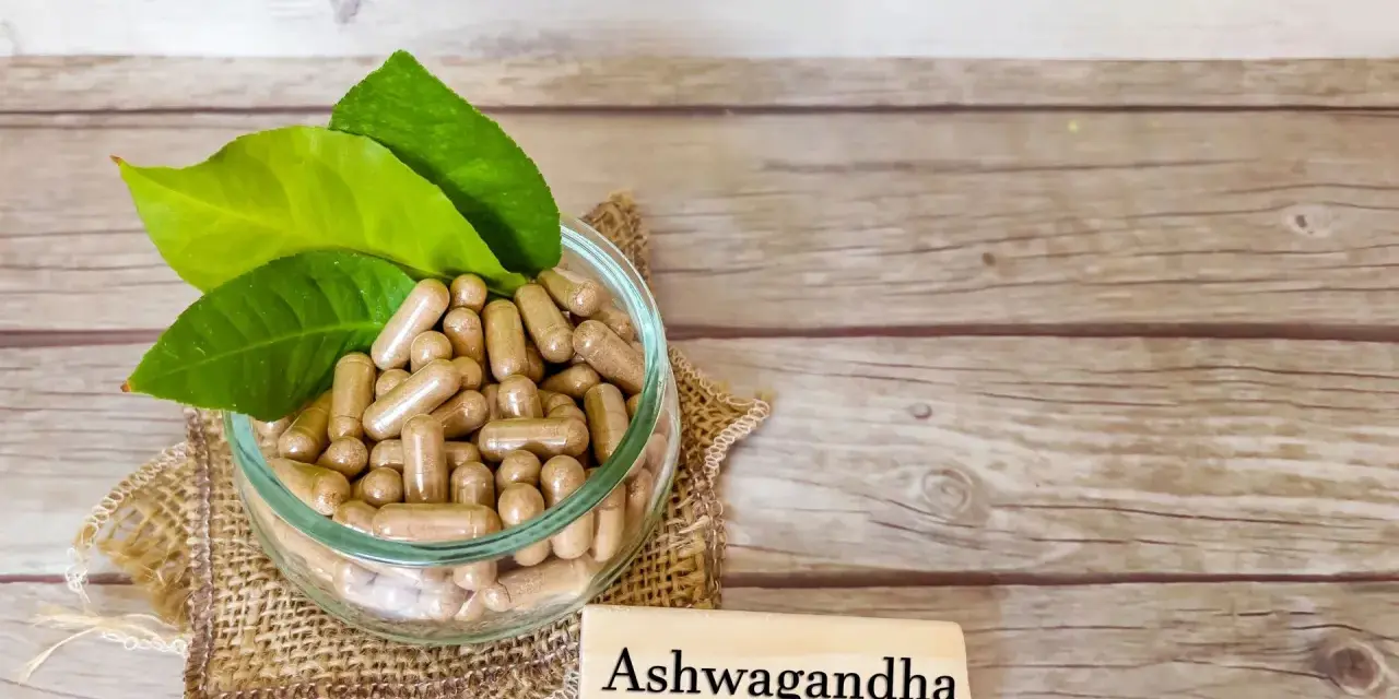 Kapsułki z ashwagandhą w szklanej misce, obok tabliczki z napisem "Ashwagandha". Warto pamiętać o potencjalnych ashwagandha skutki uboczne.