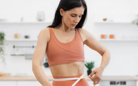 Kobieta w sportowym stroju mierzy talię, ciesząc się efektami diety low carb.