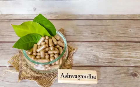 Kapsułki z ashwagandhą w szklanej misce, obok tabliczki z napisem "Ashwagandha". Warto pamiętać o potencjalnych ashwagandha skutki uboczne.