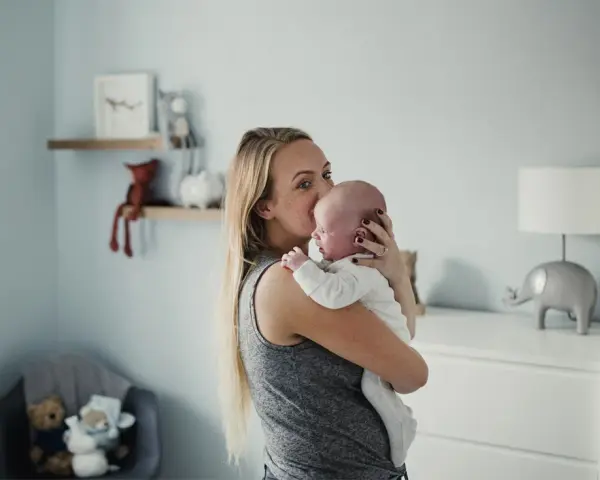Mama tuli noworodka, by ukoić jego czkawkę. W tle pokój dziecięcy z pluszakami.