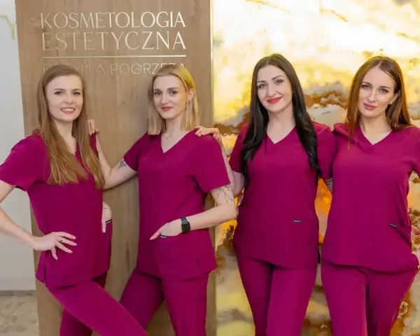 Cztery kobiety w uniformach medycznych stoją obok siebie przed tablicą z napisem "Kosmetologia Estetyczna".