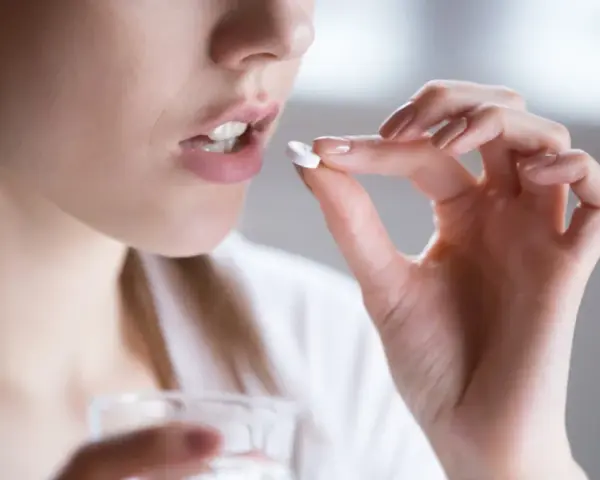 Kobieta bierze tabletkę clindamycin mip 600 na infekcje bakteryjne.