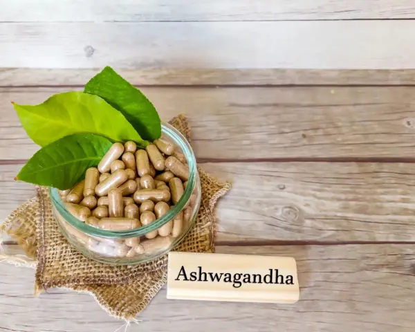 Kapsułki z ashwagandhą w szklanej misce, obok tabliczki z napisem "Ashwagandha". Warto pamiętać o potencjalnych ashwagandha skutki uboczne.
