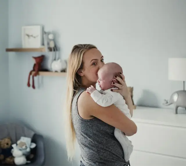 Mama tuli noworodka, by ukoić jego czkawkę. W tle pokój dziecięcy z pluszakami.
