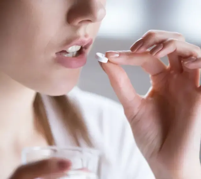 Kobieta bierze tabletkę clindamycin mip 600 na infekcje bakteryjne.