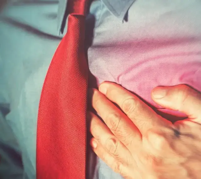 Mężczyzna w czerwonym krawacie trzyma się za serce. Ból w klatce piersiowej może być sygnałem, by skonsultować się z lekarzem, który może zalecić np. concor cor.