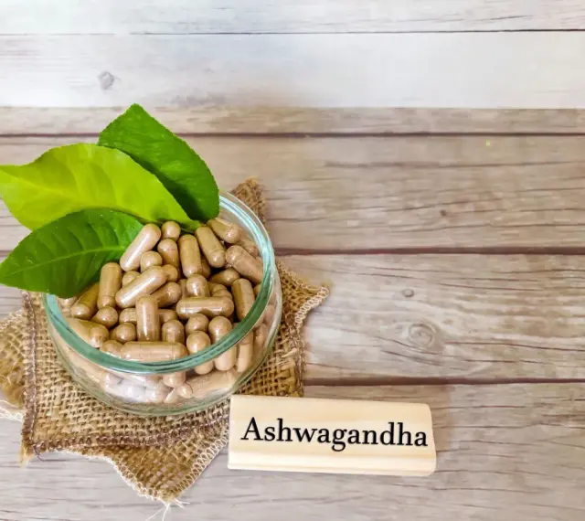 Kapsułki z ashwagandhą w szklanej misce, obok tabliczki z napisem "Ashwagandha". Warto pamiętać o potencjalnych ashwagandha skutki uboczne.