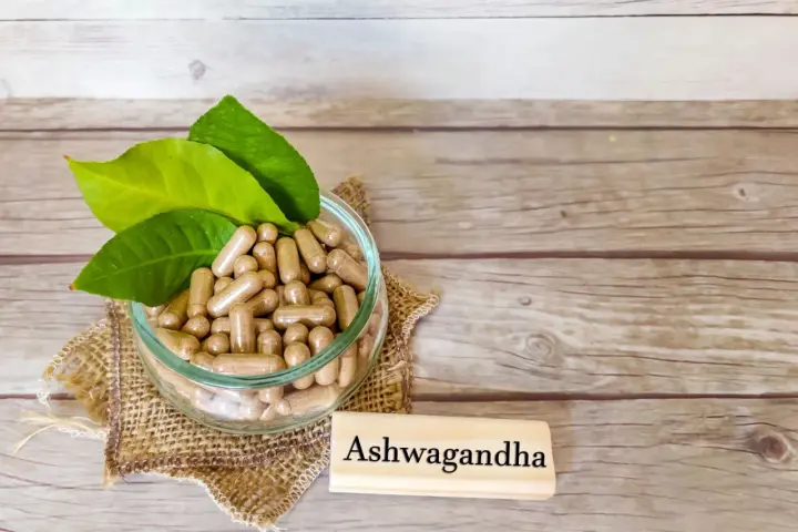 Kapsułki z ashwagandhą w szklanej misce, obok tabliczki z napisem "Ashwagandha". Warto pamiętać o potencjalnych ashwagandha skutki uboczne.