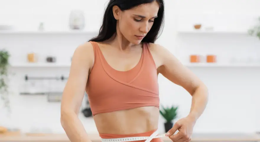 Kobieta w sportowym stroju mierzy talię, ciesząc się efektami diety low carb.