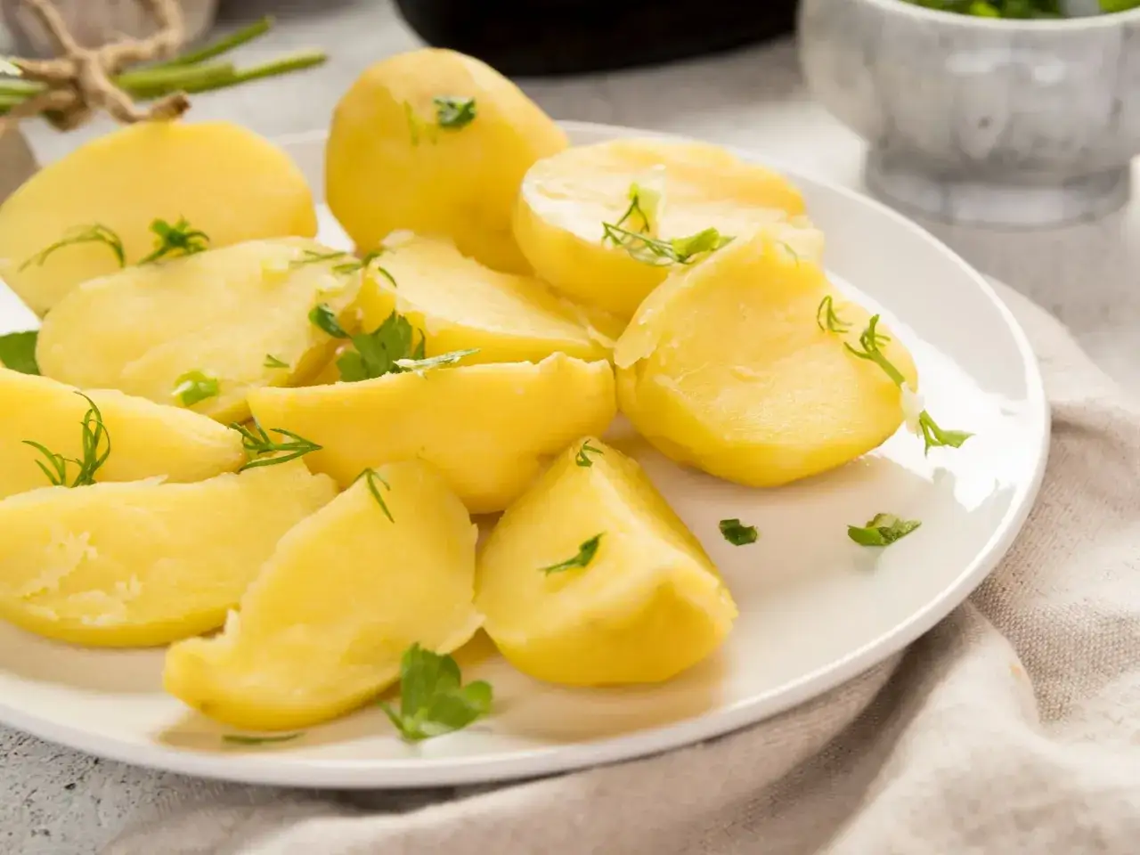 Parowane ziemniaki z koperkiem i natką pietruszki na białym talerzu. Zdrowe i niskokaloryczne ziemniaki kcal.