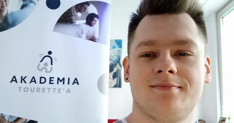 Mężczyzna z tatuażem na uchu obok logo "Akademia Tourette'a".
