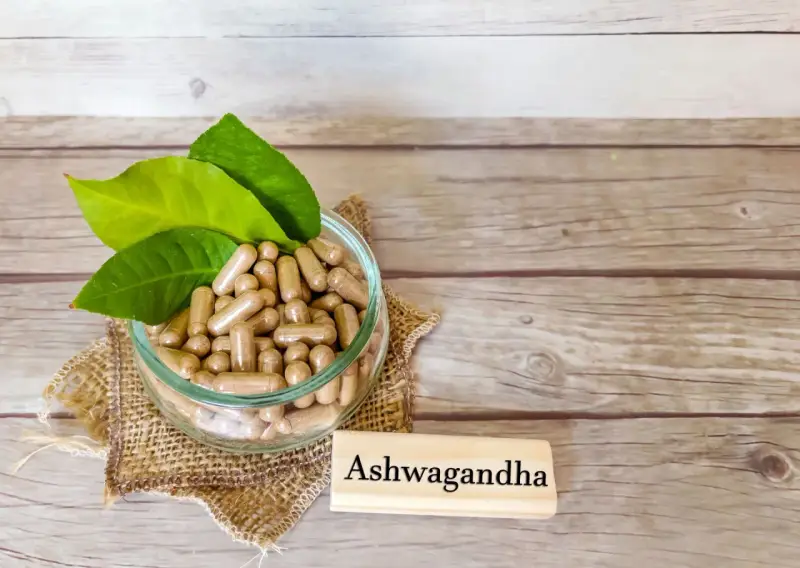 Kapsułki z ashwagandhą w szklanej misce, obok tabliczki z napisem "Ashwagandha". Warto pamiętać o potencjalnych ashwagandha skutki uboczne.